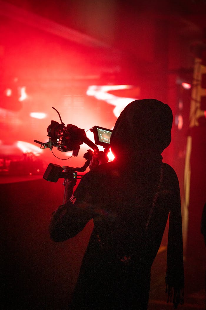 Silhouette of a person filming with a camera in a vibrant red-lit environment.