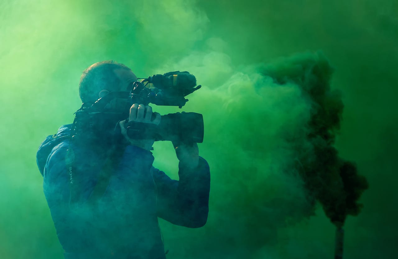 A professional cameraman captures footage surrounded by striking green smoke, highlighting filmmaking elements.