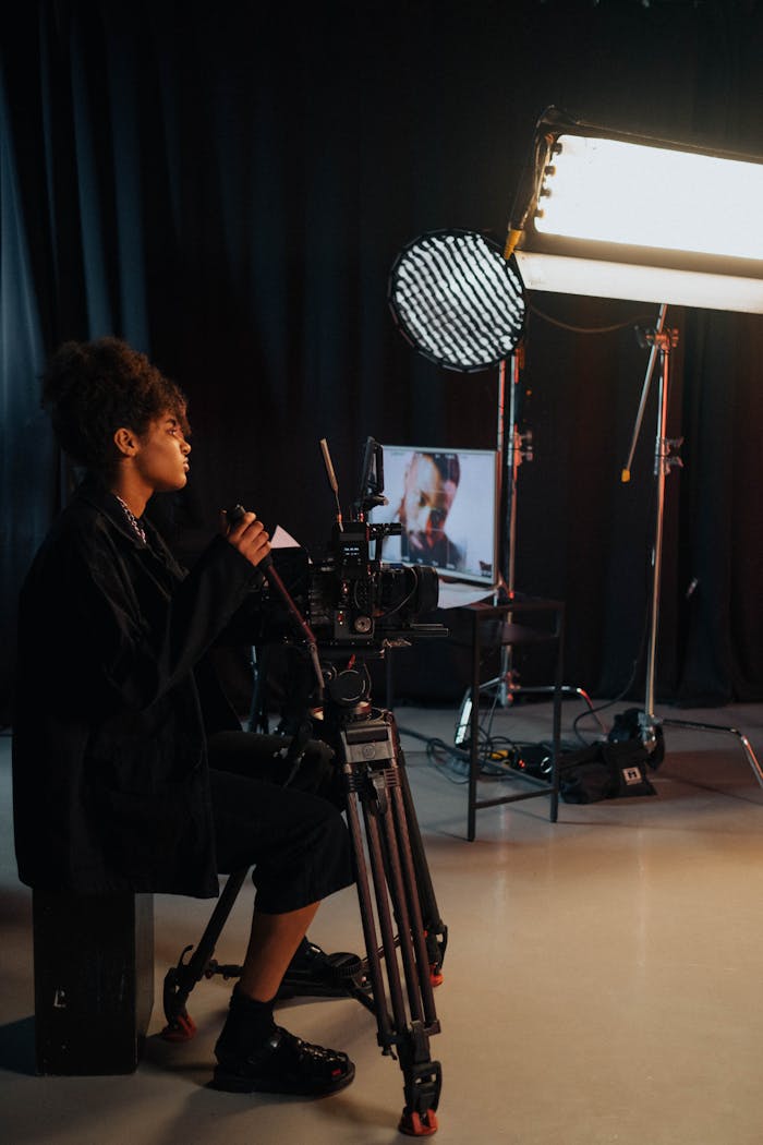 Videographer operating camera in a dark studio with lighting equipment and monitors.